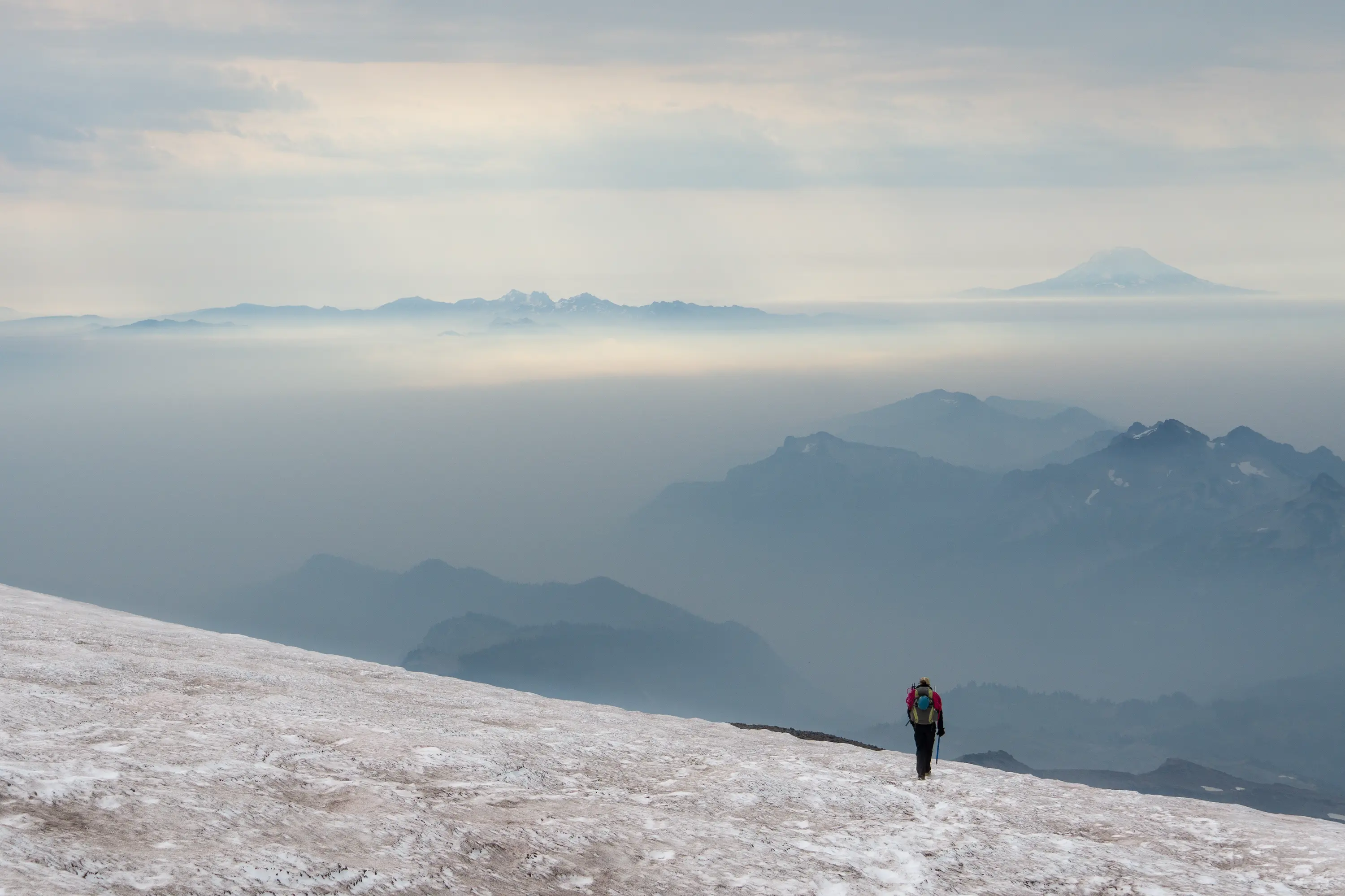 A friend walking down the Muir Snowfield on Mt. Rainier. Tatoosh Range, Goat Rocks, and Mt. Adams rise from a sea of wildfire smoke.